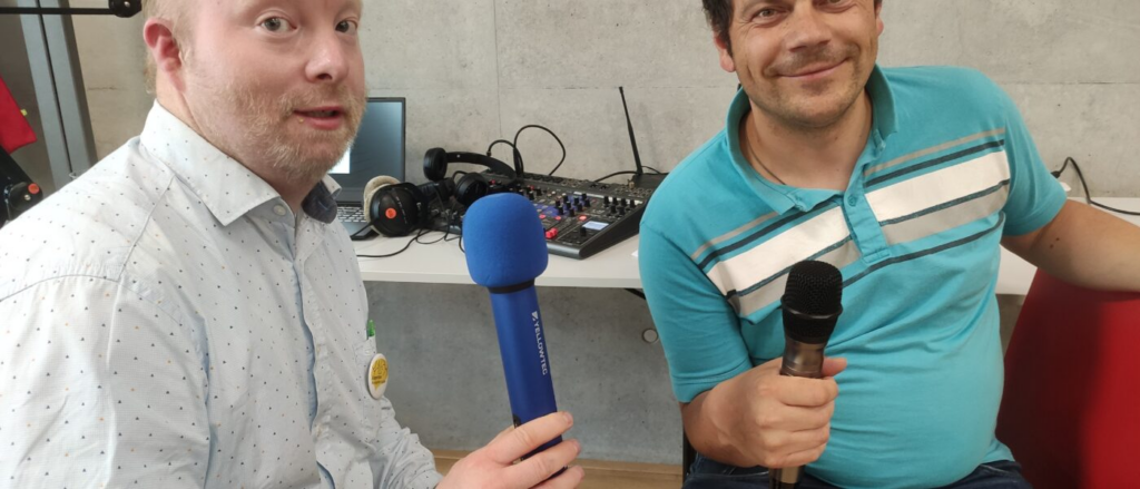 Zwei Personen vor einem Mischpult mit Mikrofonen in der Hand